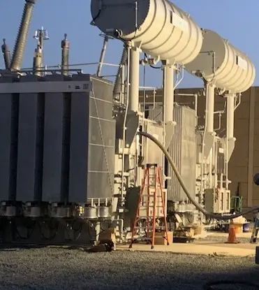 A large electrical power transformer on top of a cement field.